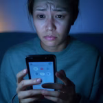 A síndrome do impostor no namoro on-line: como superar aquela voz que lhe diz que você não é suficiente pessoa olhando para o smartphone com expressão ansiosa, interface de deslizamento brilhando na tela, dúvida